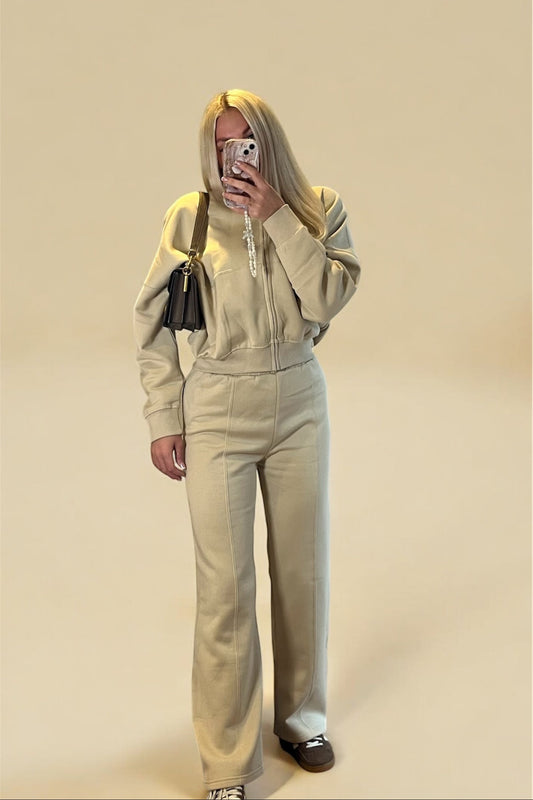 Person wearing a beige outfit with a matching jacket and pants, standing against a beige background.