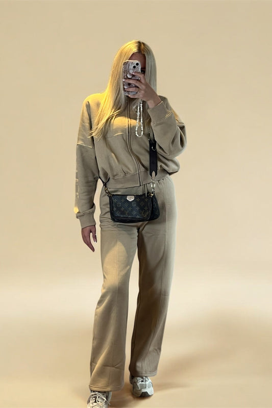 Person wearing a beige tracksuit with a black handbag on a beige background