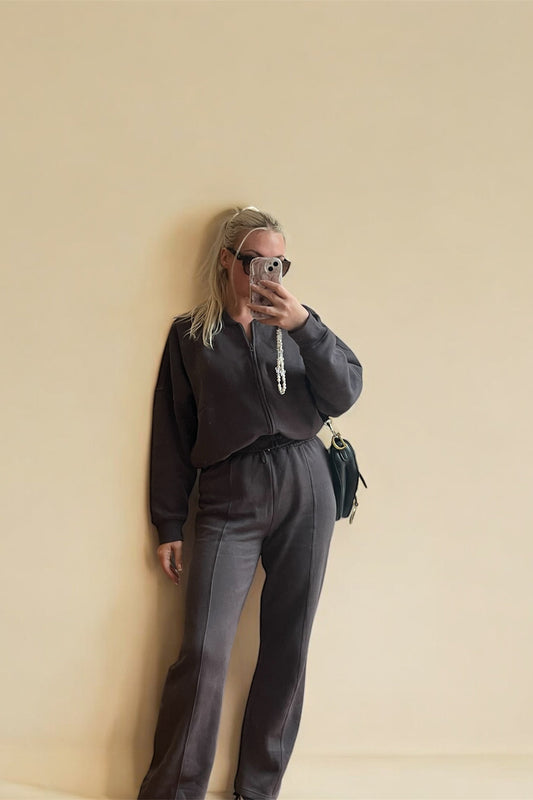 Person wearing a dark gray outfit against a beige wall