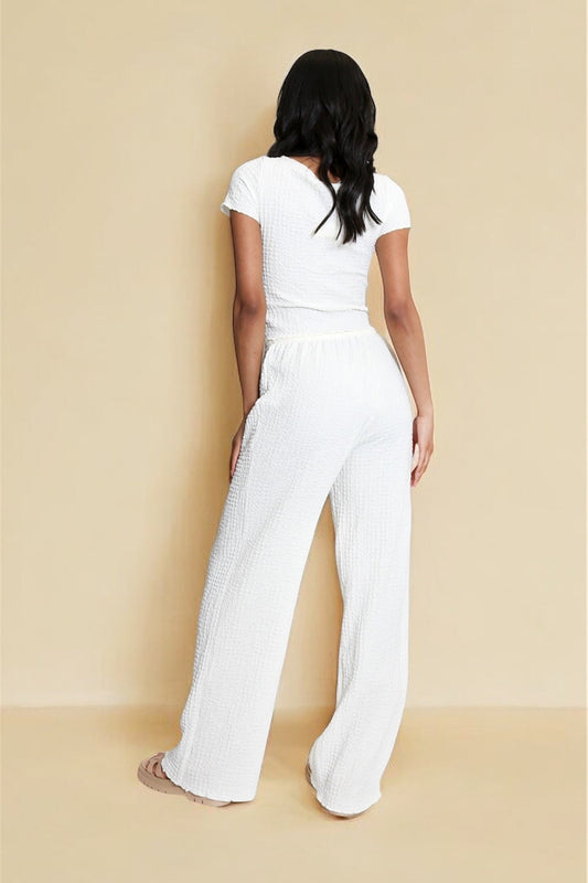 Person wearing a white outfit standing against a beige background